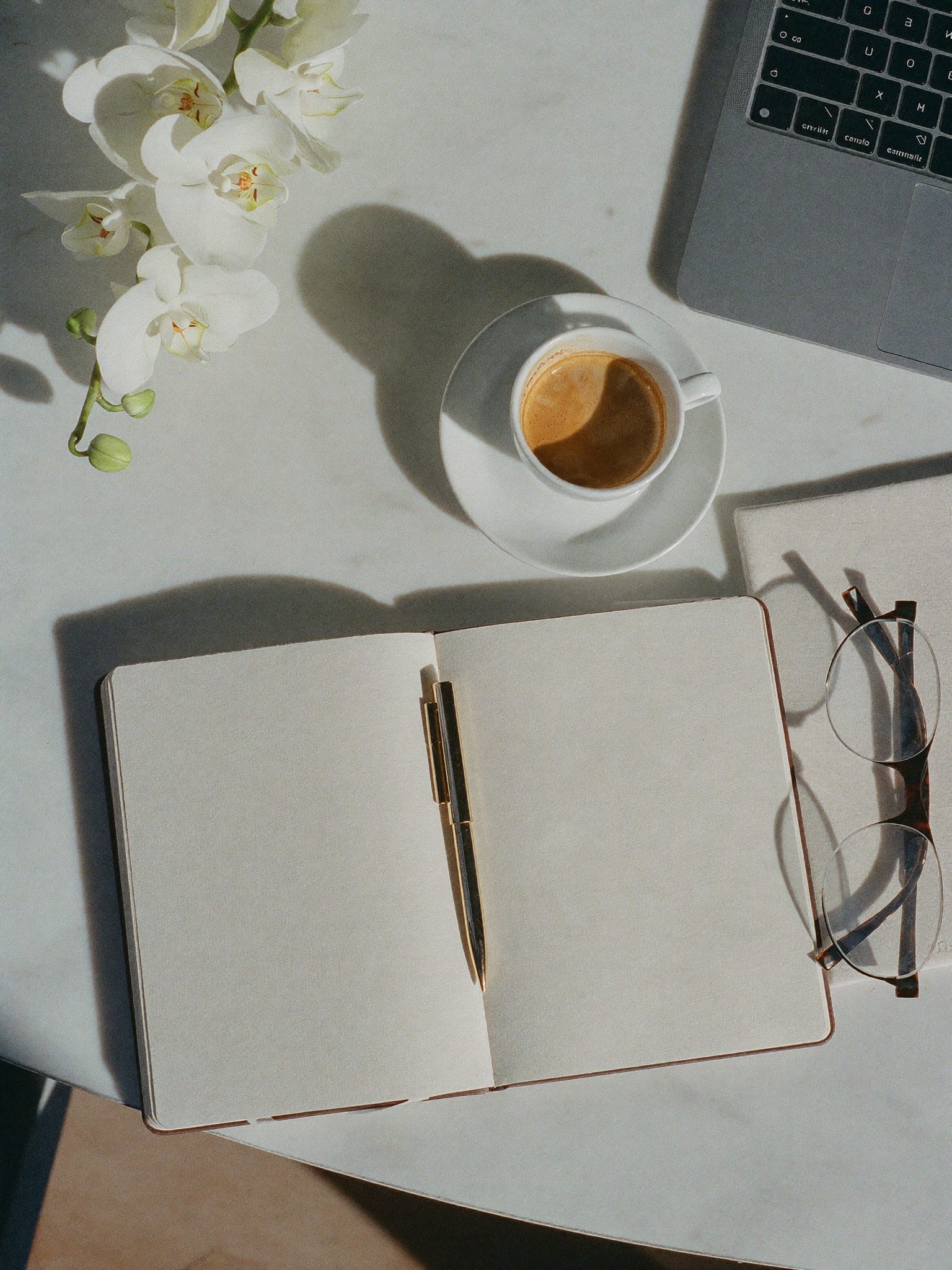 Aufgeräumter heller Schreibtisch mit Notizbuch, goldenem Stift und Espresso